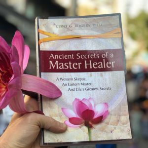 Ancient Secrets of a Master Healer book held with a lotus blossom.